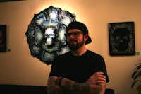 Robert Hamilton, a Carrollton artist and a University of North Texas graduate, stands in front of one of his new creations, “Blue flower and sugar skull,” at Wine2 on Thursday in Denton. Hamilton’s style — bright colors and loose lines inspired by tattoos and by Dia De Los Muertos folk art — established the aesthetic of Denton’s Day of the Dead Festival. <137>The exhibit at the local wine shop is the official beginning of Denton’s Day of the Dead for the artist.<137>Lucinda Breeding
