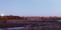 The lights of Robson Ranch shine just after dusk across a field from a compressor station and gas wells near Ponder on Thursday.